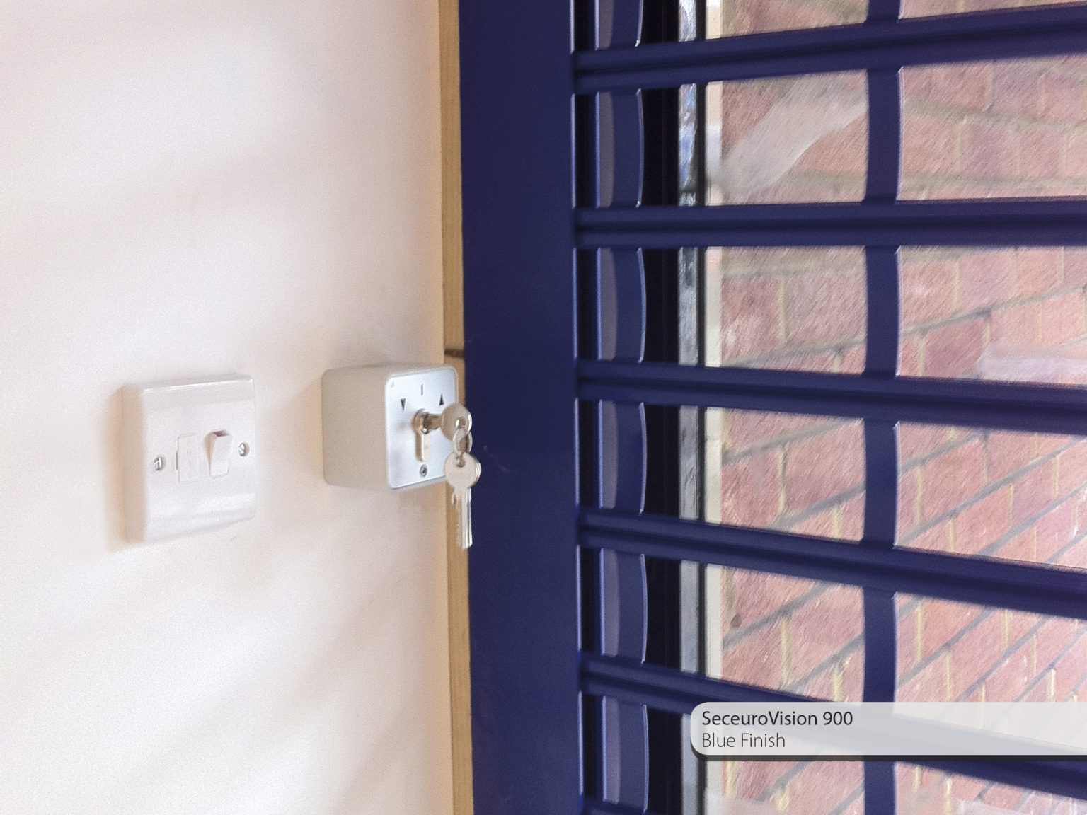 A white wall with a light switch and a lockbox holding keys. Adjacent is a window with blue metal bars. The label reads "SeceuroVision 900 Blue Finish.